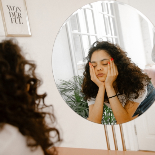 A woman looking tired exhausted and sad in the mirror because she has low self worth