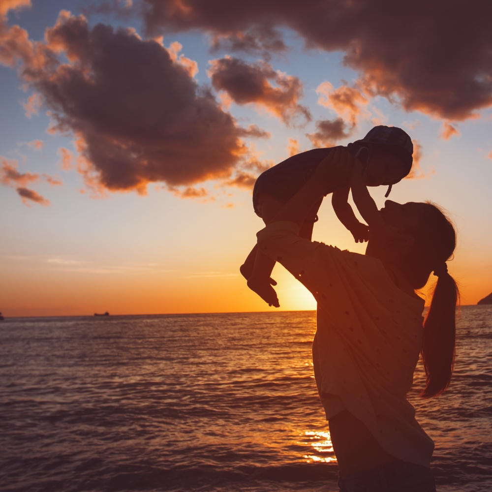 mother holding her baby infront of a sunset