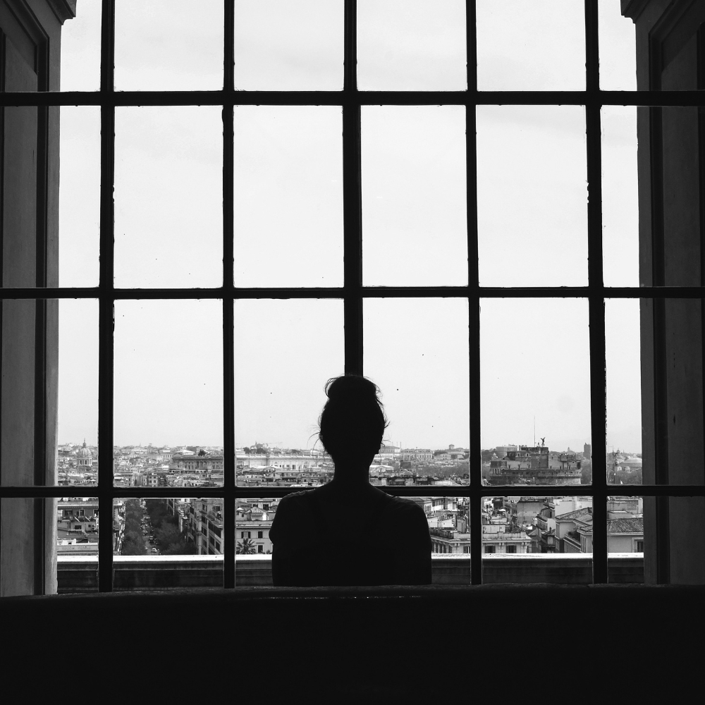 a woman looking out of a large window, she feels isolated due to past trauma
